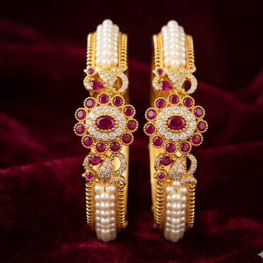 Gold bangles with pearls and red stones on a dark red fabric background