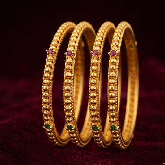 Three gold bangles with embedded gemstones on a dark background