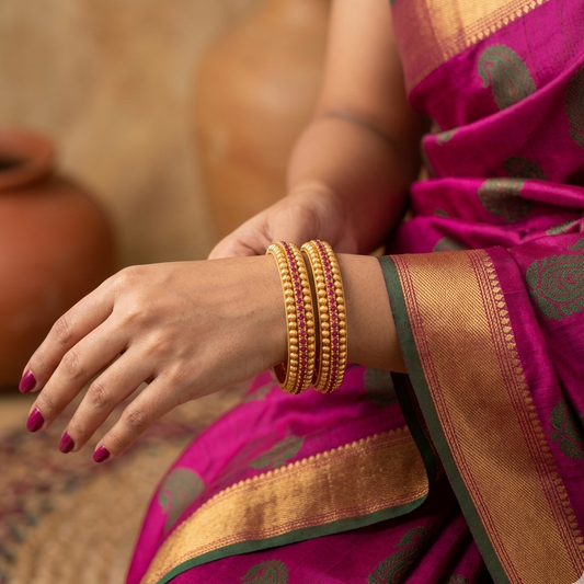 Close-up of a hand wearing gold bangles with a pink saree in the background