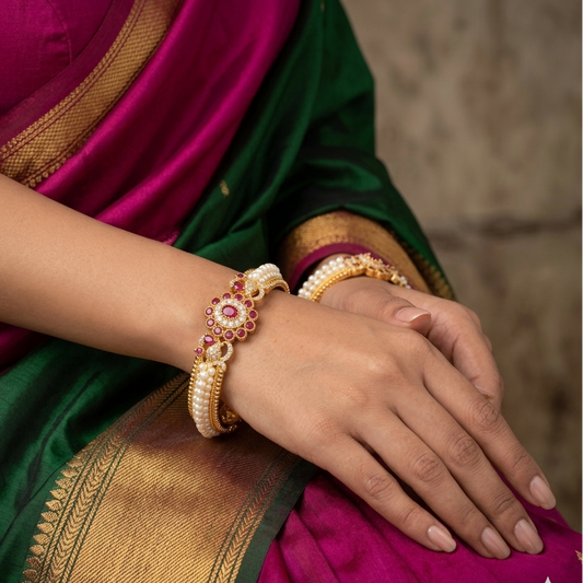 Close-up of a person wearing gold and pink bangles with a green and purple saree.