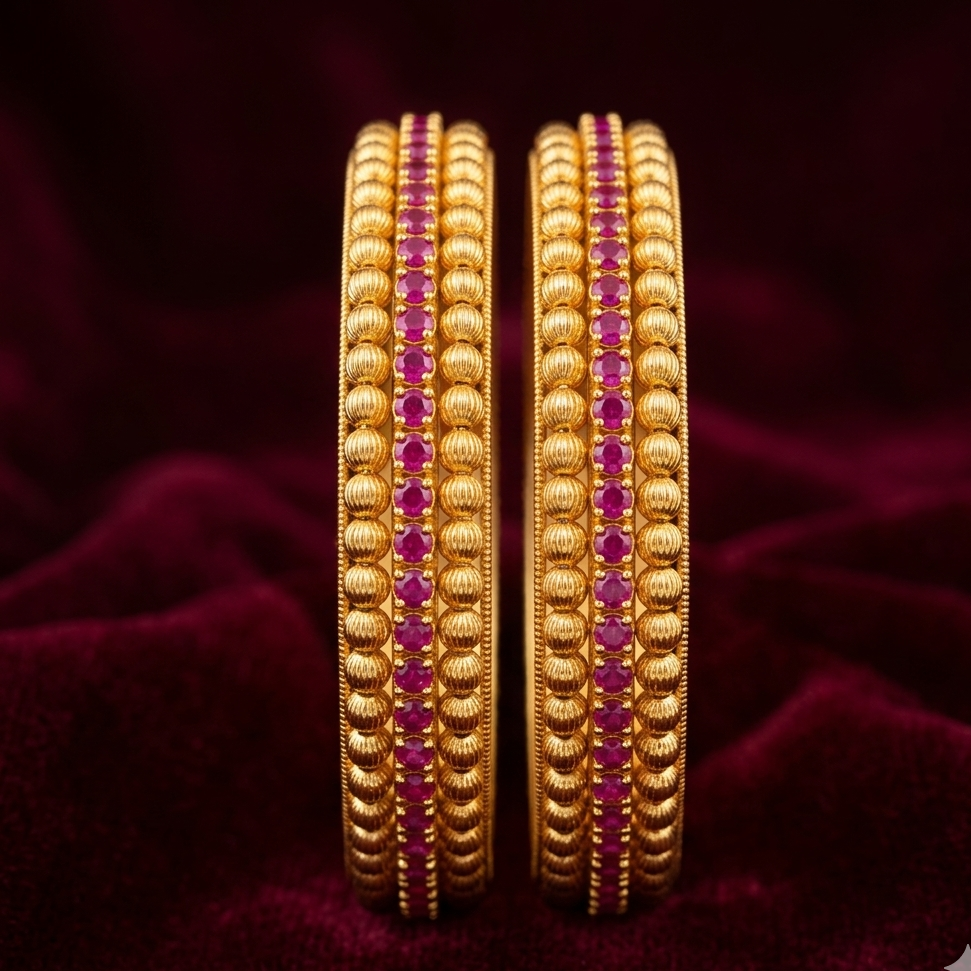 pair of gold bangles with red stones on a dark purple fabric background