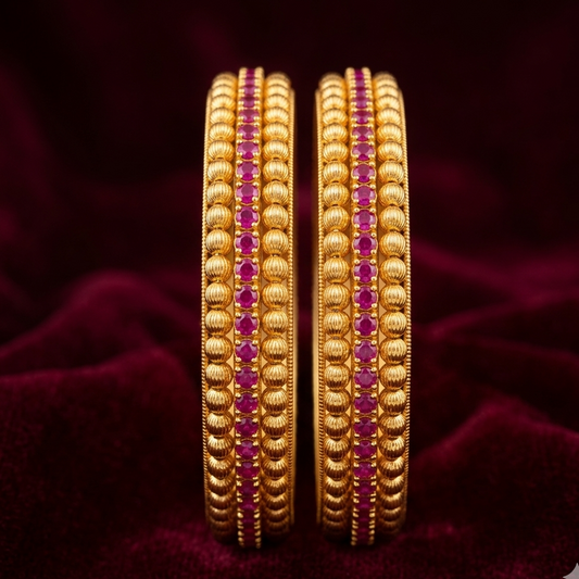Pair of gold bangles with red stones on a dark purple fabric background