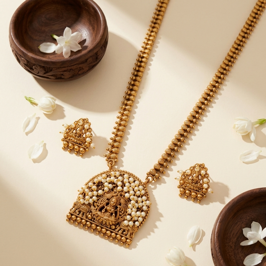 Gold necklace and earrings on a beige surface with wooden bowls and white flowers.