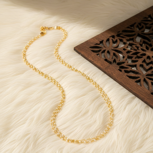 Gold necklace on a textured beige surface with a wooden decorative element.