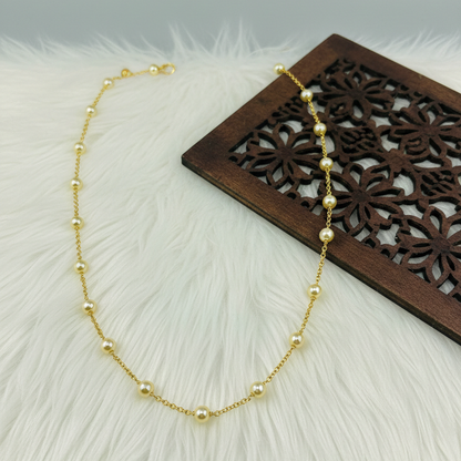 Gold necklace with pearls on a textured surface with a wooden decorative item.