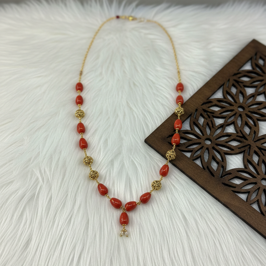 Necklace with red beads and gold accents on a textured white surface with a wooden decorative item.