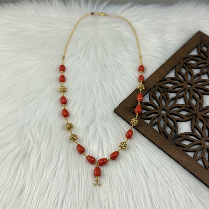 Necklace with red beads and gold accents on a textured white surface with a wooden decorative item.