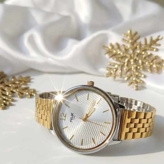 Gold watch with a white face on a white fabric background with gold snowflakes.