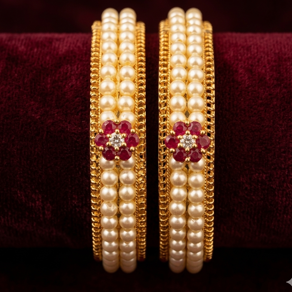 Pair of gold and pearl bangles with red gemstones on a dark background