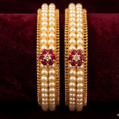Pair of gold and pearl bangles with red gemstones on a dark background