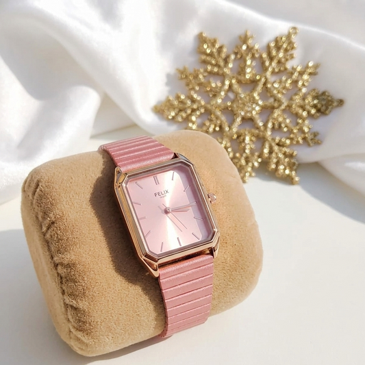 Pink watch with a matching strap on a beige cushion, with a gold snowflake decoration in the background.