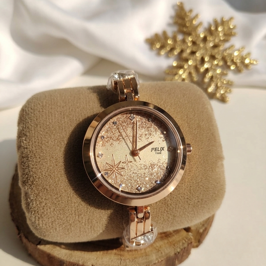 Rose gold watch with snowflake design on a beige cushion with gold snowflakes in the background
