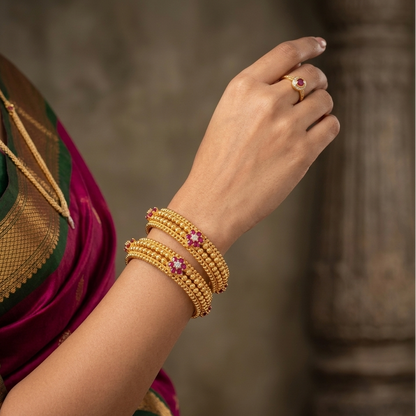 Woman's arm wearing gold bangles with pink stones, blurred background