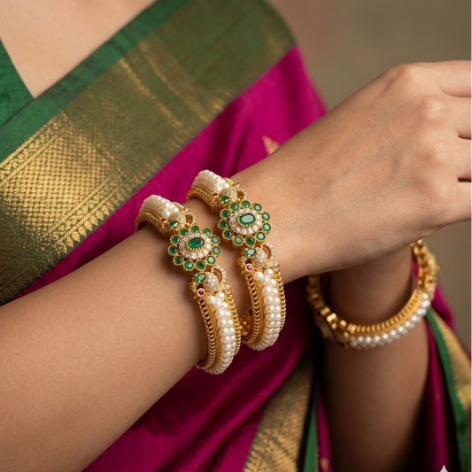 Gold and pearl bangles on a person wearing a green and pink saree.